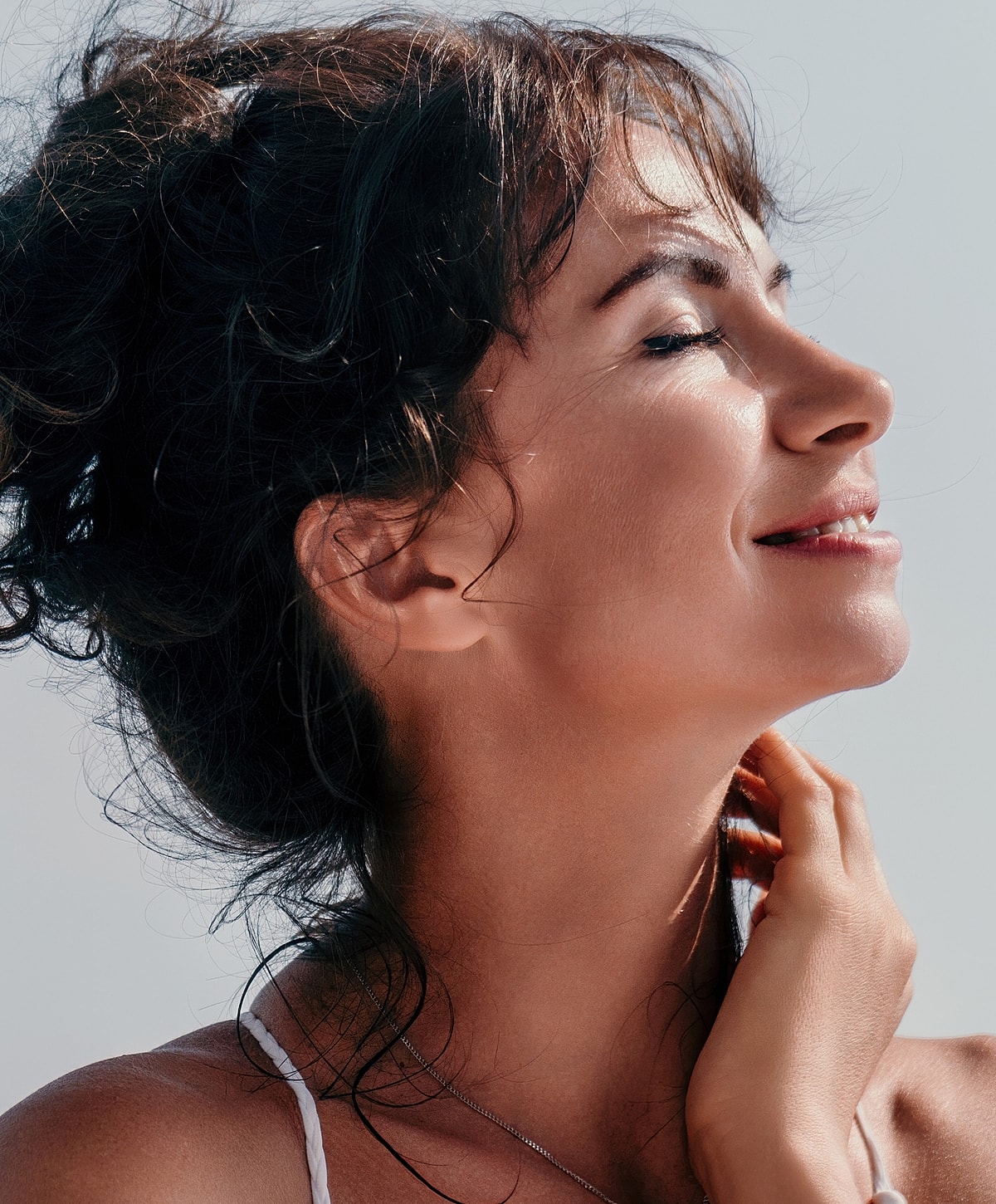 Woman smiling softly with sunlit background.