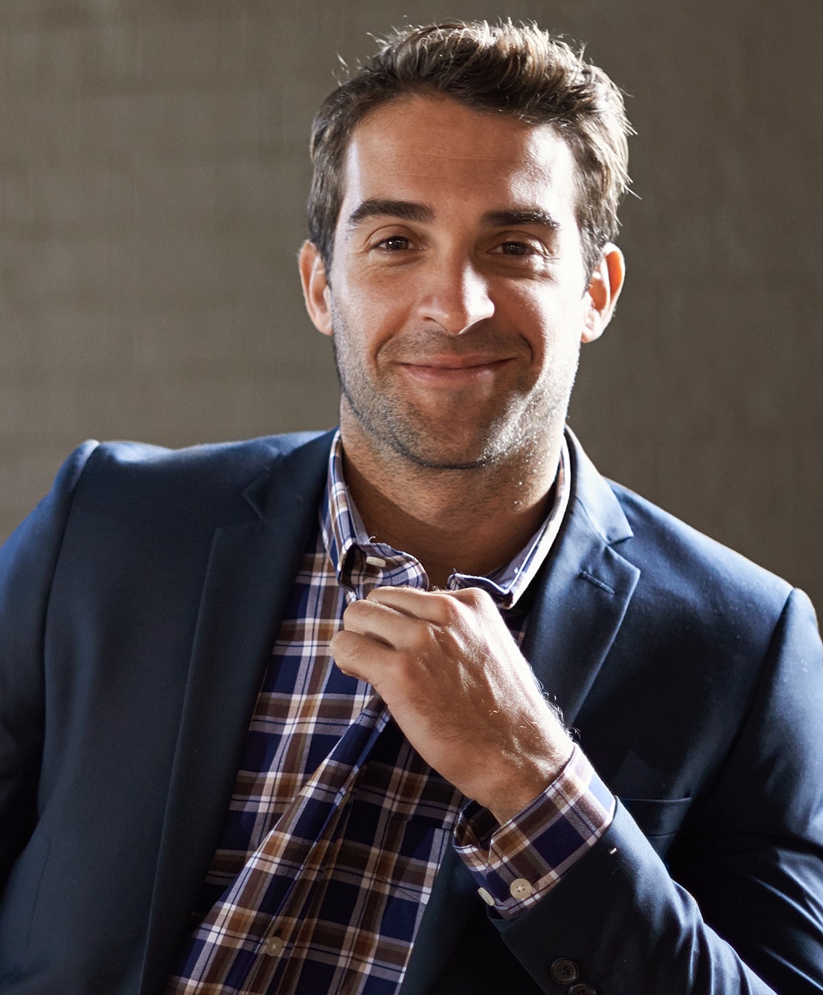 Smiling man in blazer and checkered shirt.