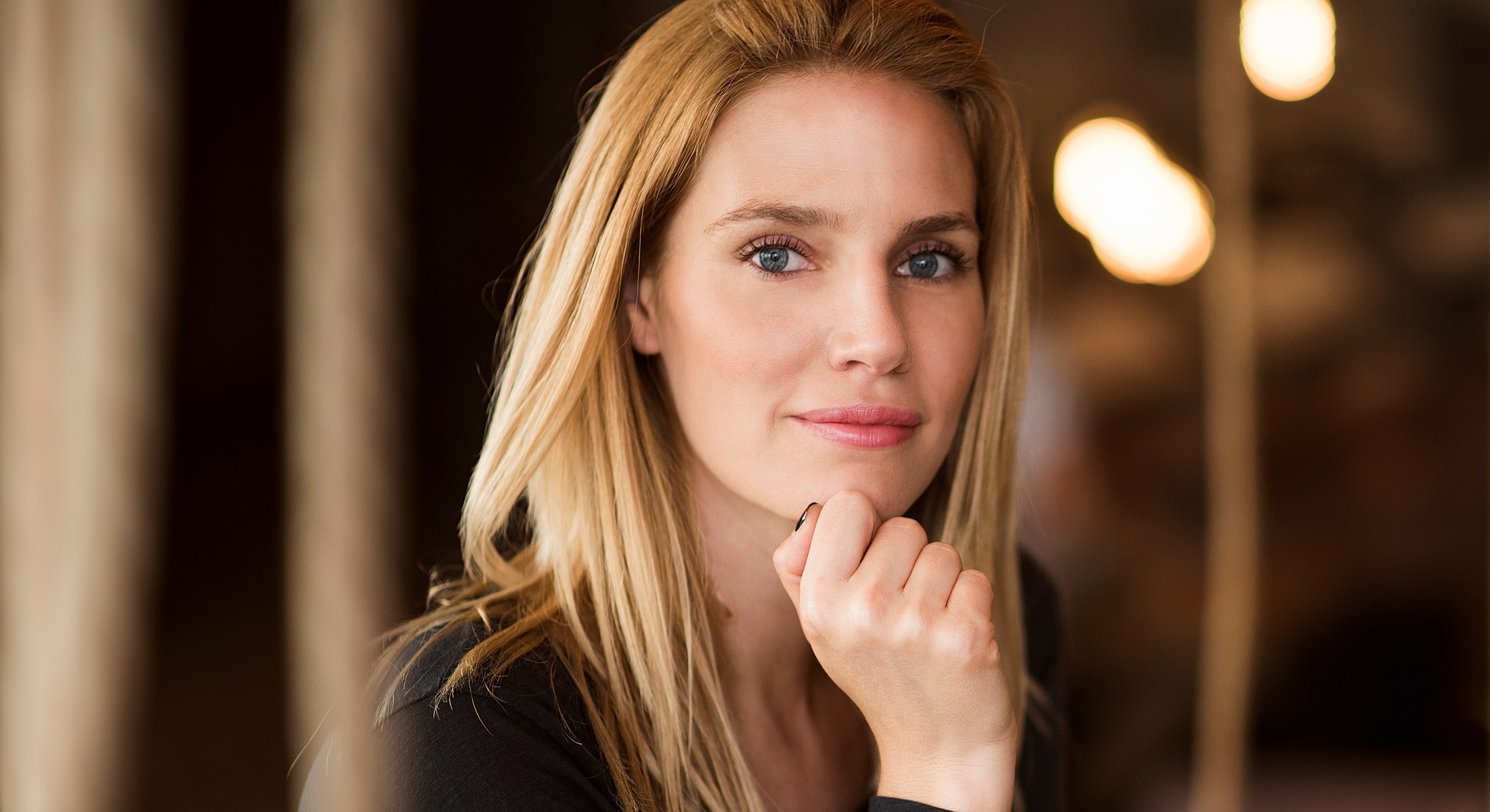 Woman with blonde hair resting chin on hand.
