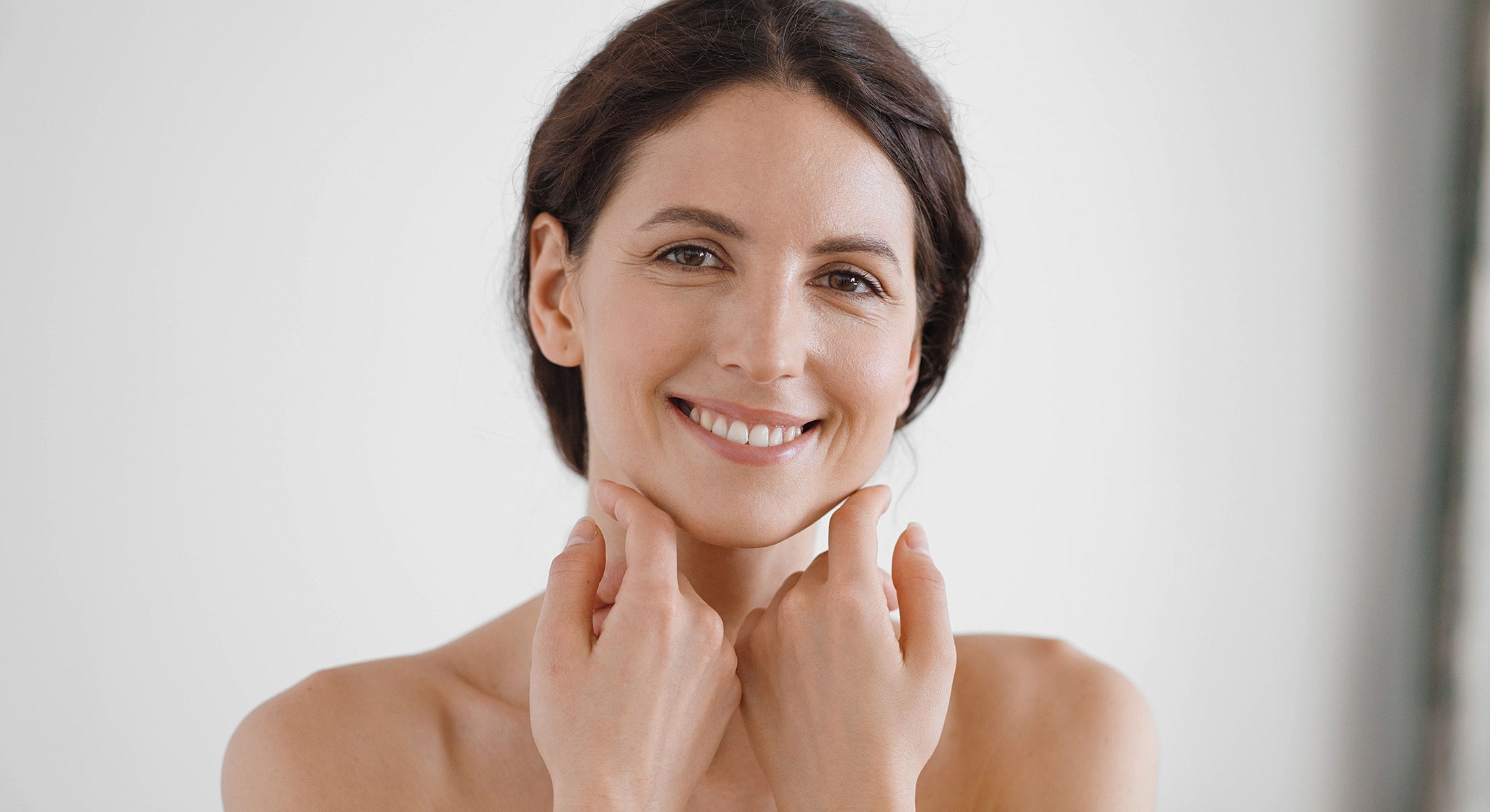 Smiling woman touching her chin and jawline.